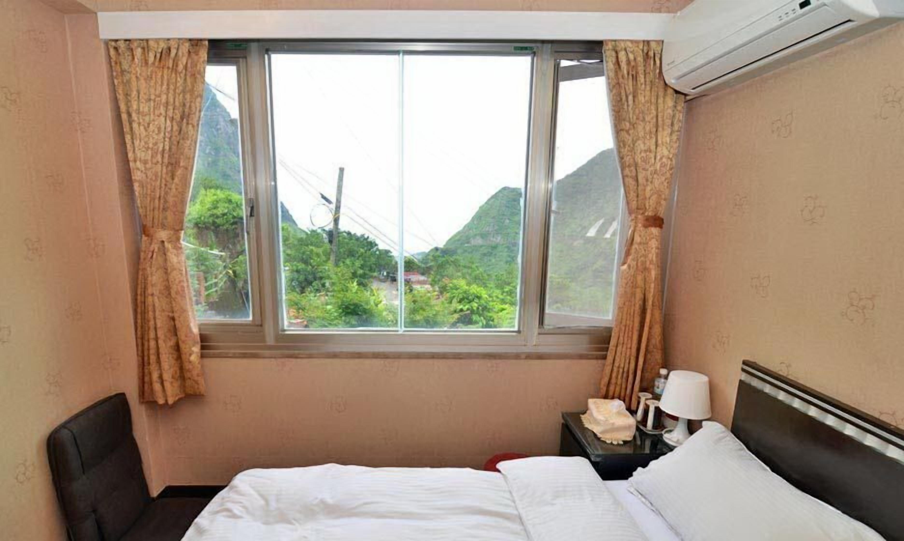 A hotel room with a bed, a nightstand, a lamp, and a window with curtains.