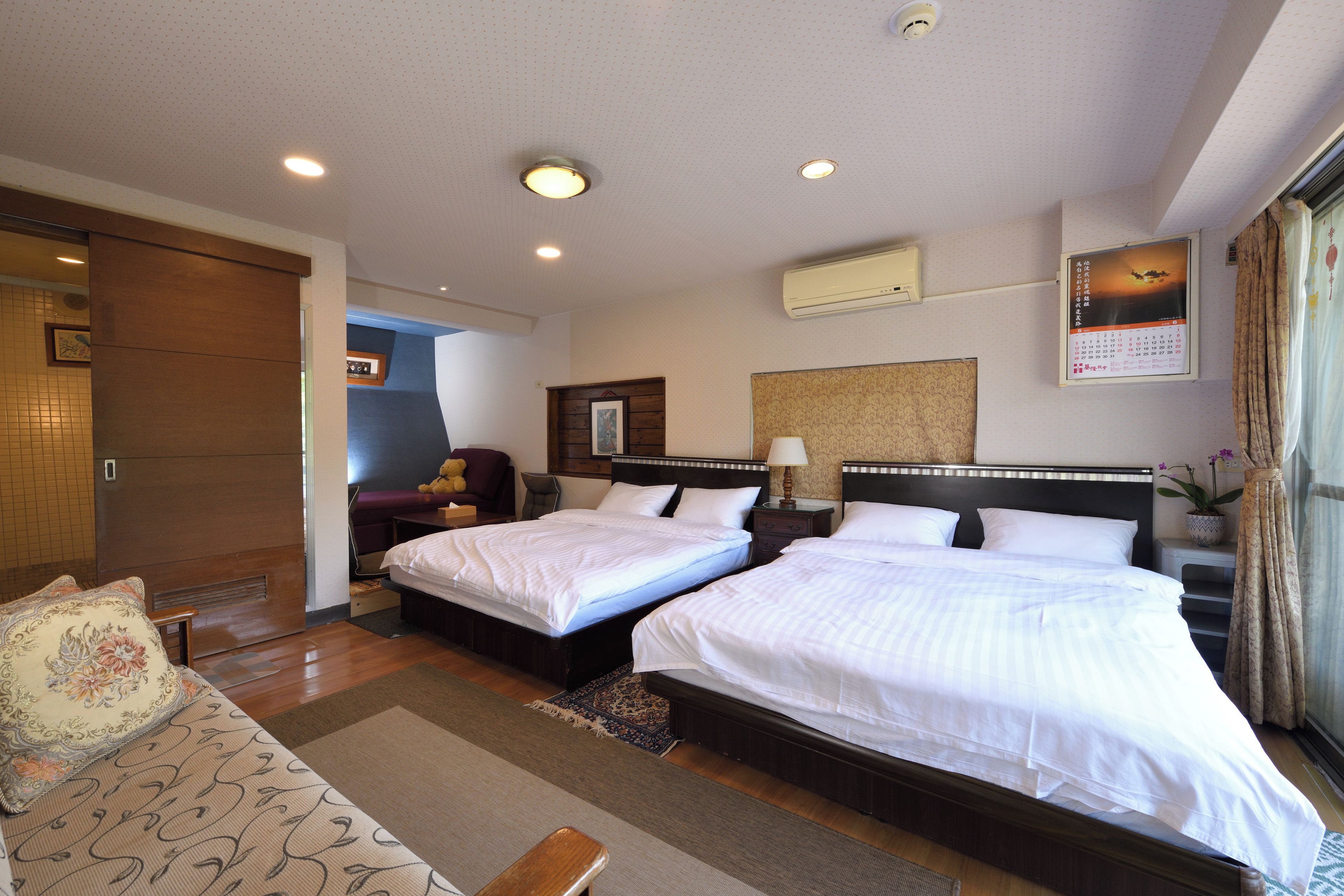 A hotel room with two beds, a sofa, a desk, and a window with curtains.