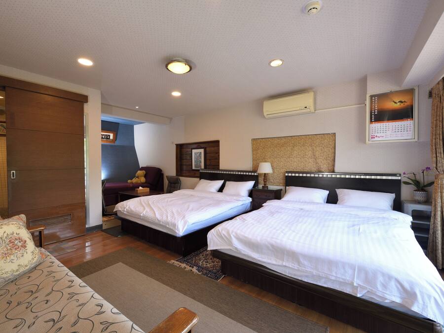 A hotel room with two beds, a sofa, a desk, and a window with curtains.