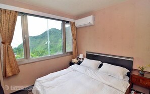A hotel room with a bed, a nightstand, a lamp, an air conditioner, and a window with curtains.