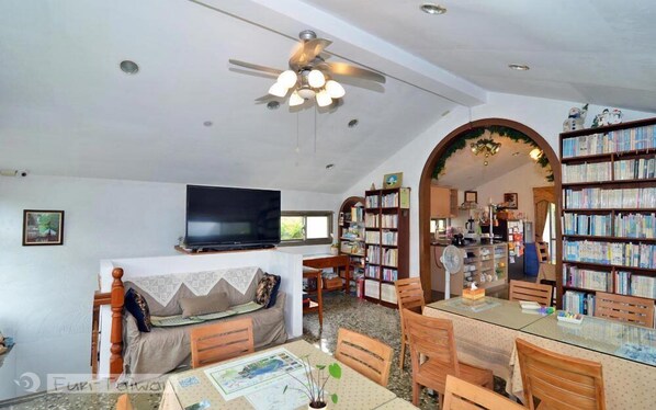 A spacious living room with a sofa, a television, a ceiling fan, and a bookshelf filled with books. - Levite Villa (New Taipei City)