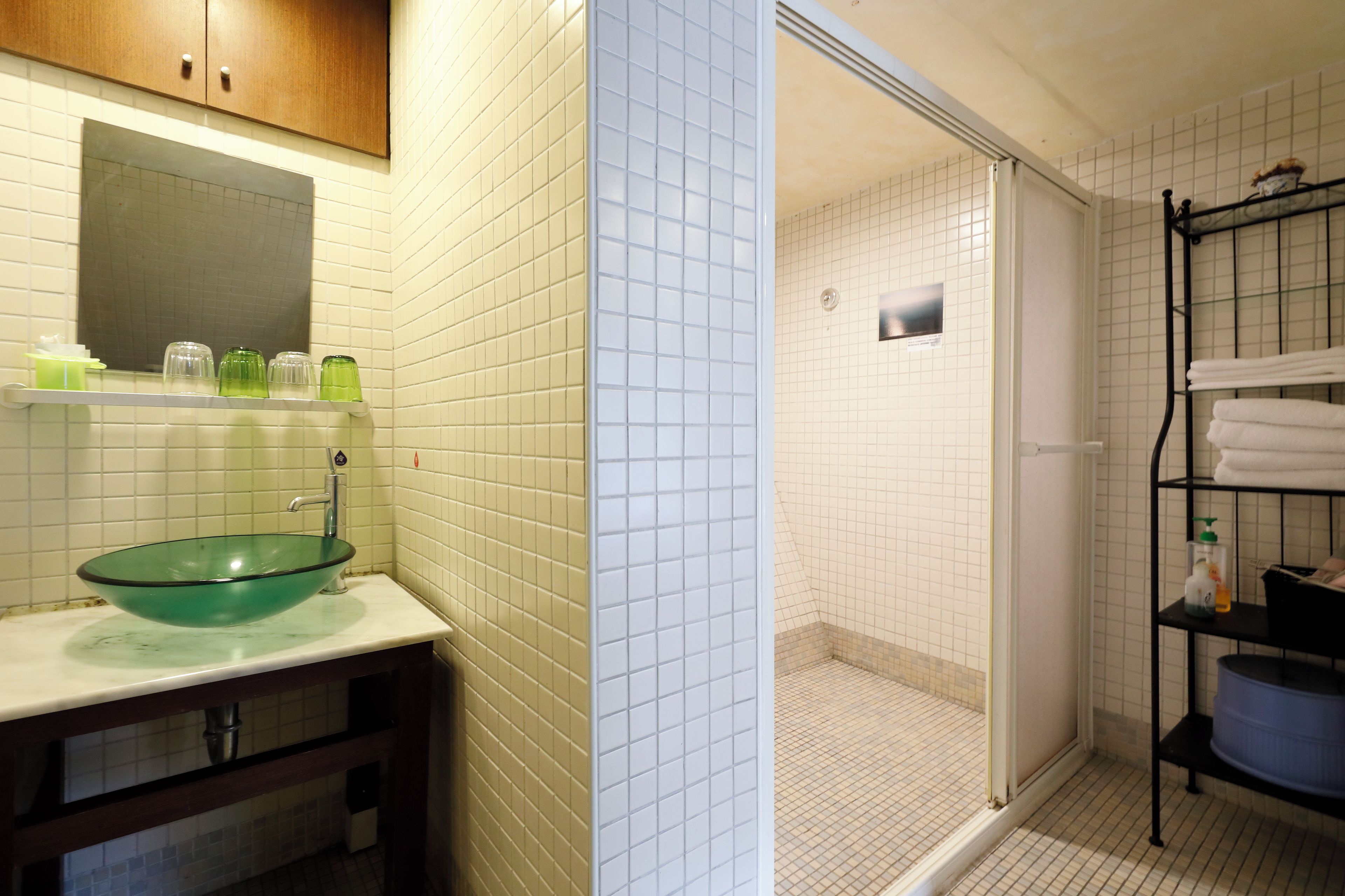 A bathroom with a glass basin sink, white tiled walls, a wooden cabinet, and a shower area with a glass door.