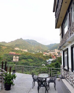 A terrace with a table and chairs, overlooking a mountainous landscape with buildings. - Levite Villa (New Taipei City)