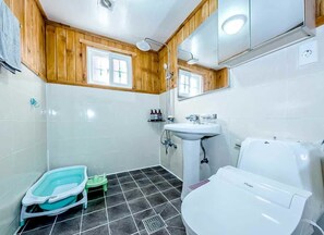 Ein Badezimmer mit einem weißen Waschbecken, einer Toilette und einer Dusche. Die Wände sind aus Holz und es gibt ein Fenster.