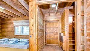 Ein Interieur einer Holzhütte mit einer Holztür, einem Fenster und einer Matratze auf dem Boden.