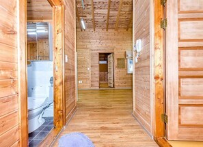 Ein Holzboden-Flur mit einem Badezimmer links, einer Tür zu einem anderen Raum rechts und einer sichtbaren Toilette im Hintergrund.