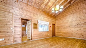 Ein großzügiger Raum mit Holzwänden und -böden, einem großen Fenster mit Vorhängen sowie einer Decke mit freiliegenden Balken und Pendelleuchten.