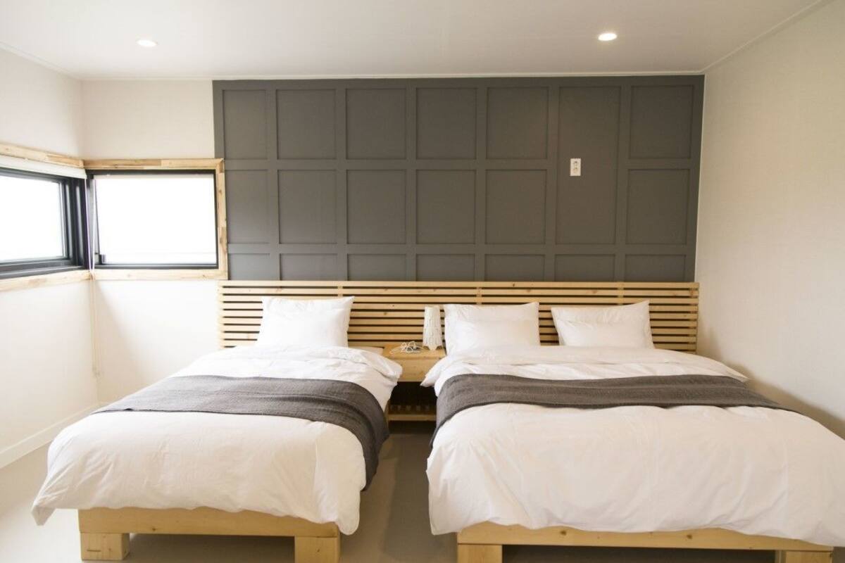 A bedroom with two single beds, a wooden headboard, and a window with blinds.