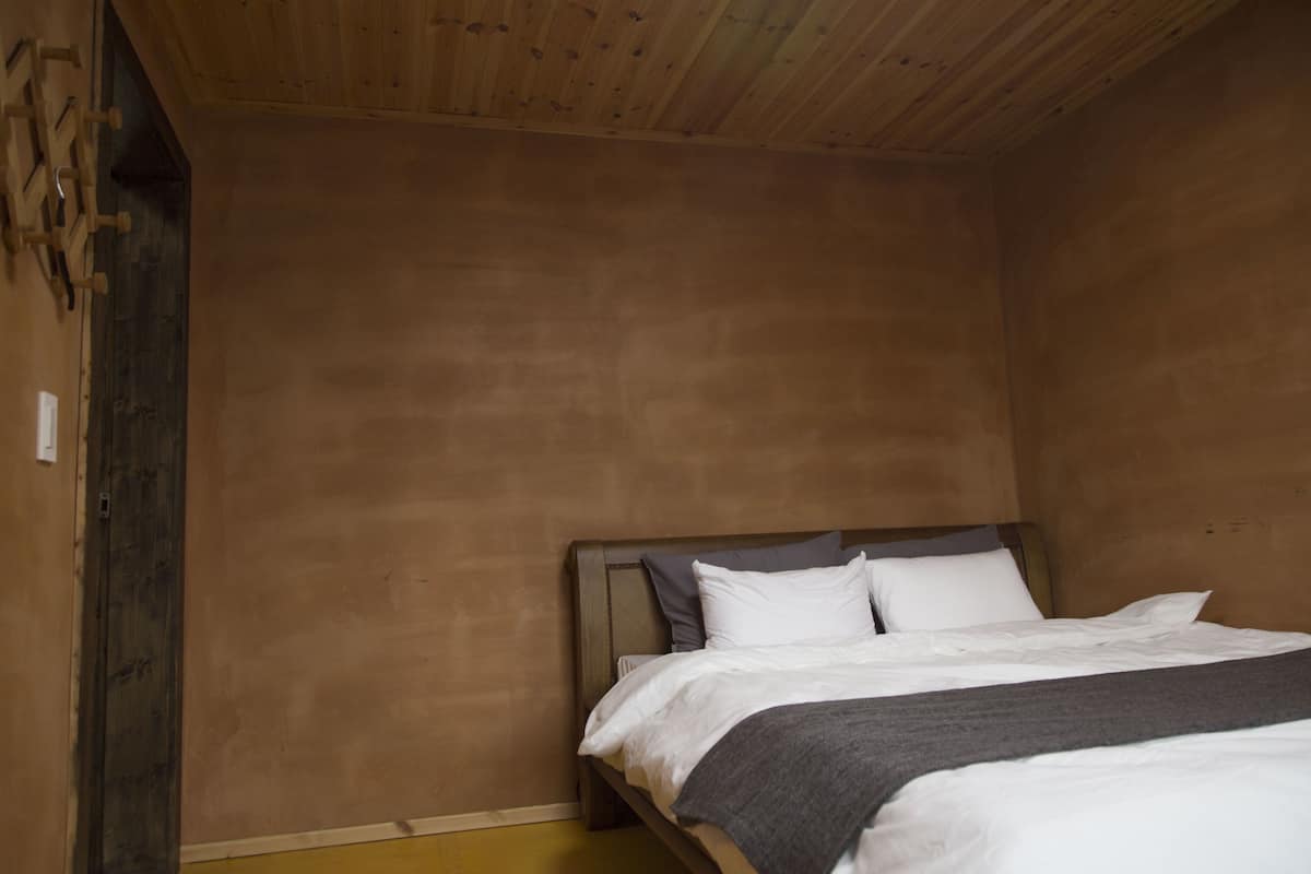 A bedroom with a wooden bed frame, white bedding, and a wooden ceiling.