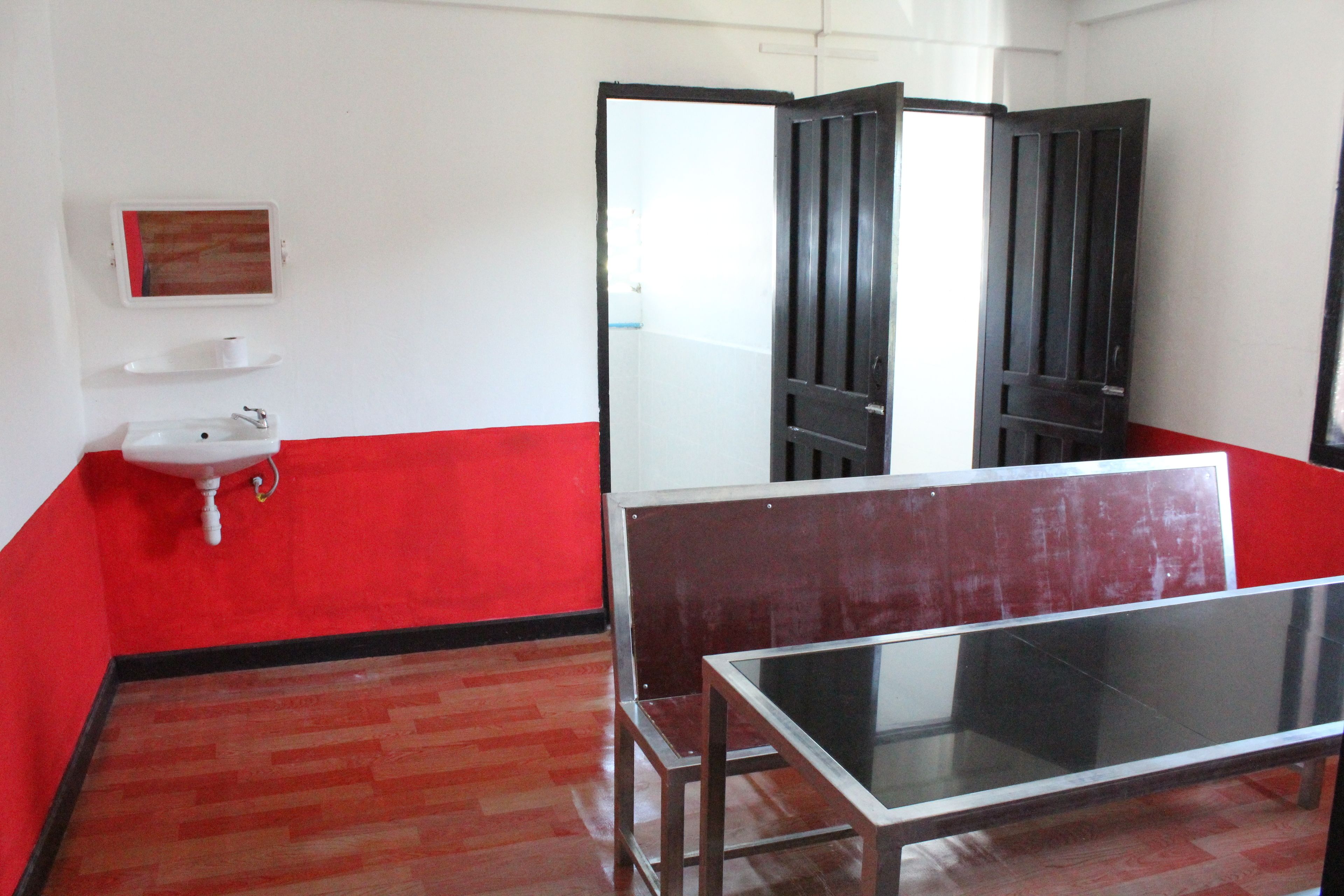 A room with a red and white color scheme, a white sink, a glass table, and a mirror on the wall.