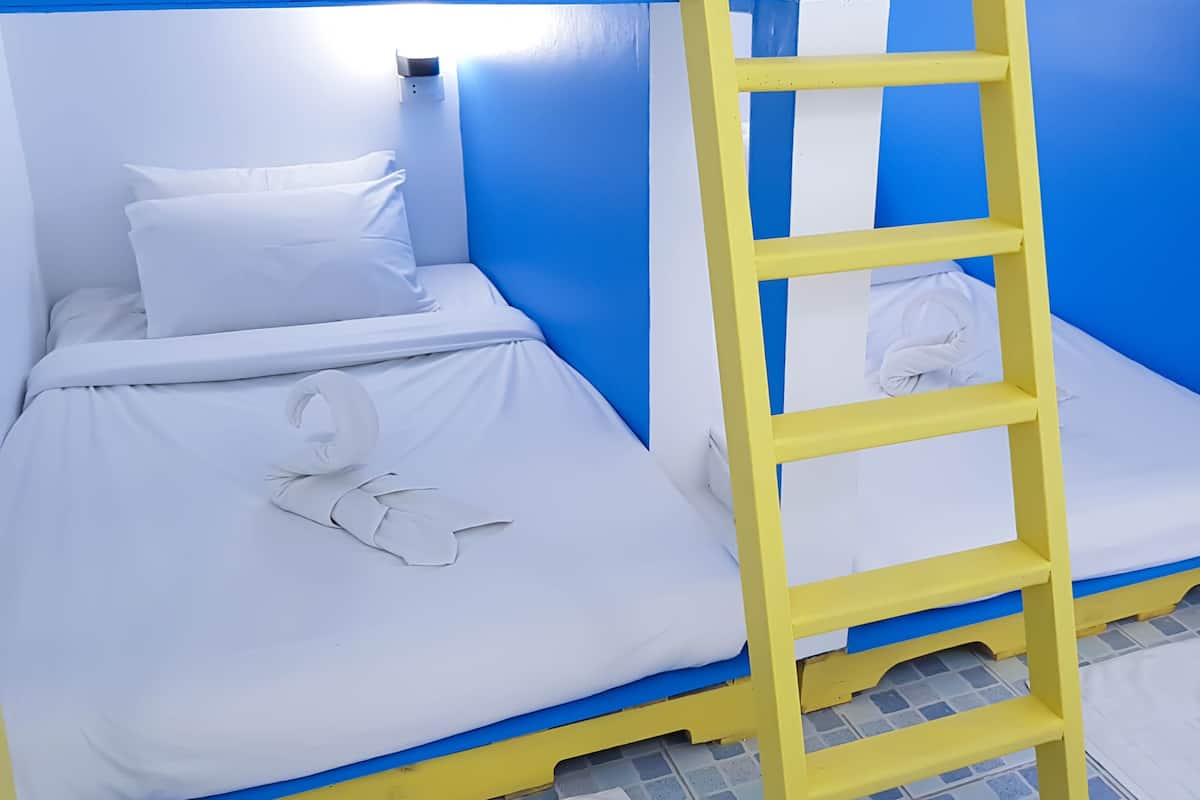Cama litera con ropa blanca y escalera amarilla.