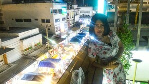 A woman standing at a balcony overlooking a busy outdoor market with various stalls and people. - Hua Hin Night Market Hostel (Hua Hin)
