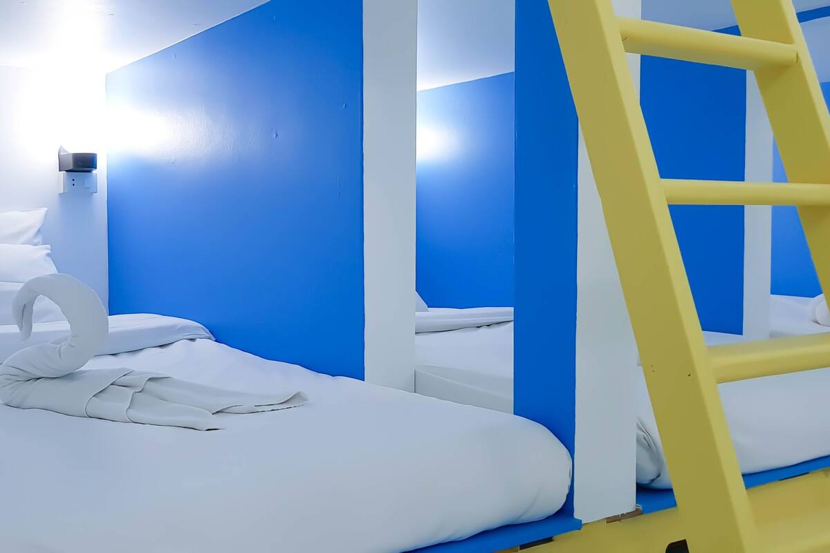 Habitación con literas, escalera amarilla y ropa de cama blanca.