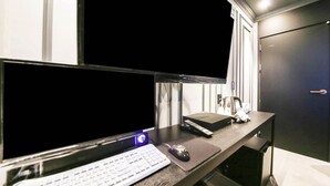 Une chambre d’hôtel moderne équipée d’un bureau, de deux écrans, d’un clavier et d’une souris.