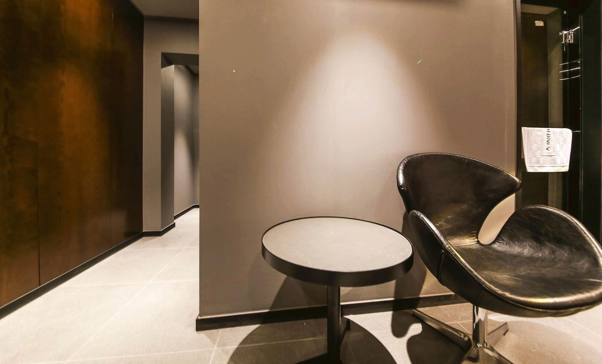 A modern interior with a round table and a single black leather chair.