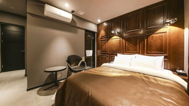 Une chambre d’hôtel avec un lit, une chaise, une petite table, un lambris en bois et un appareil de climatisation.