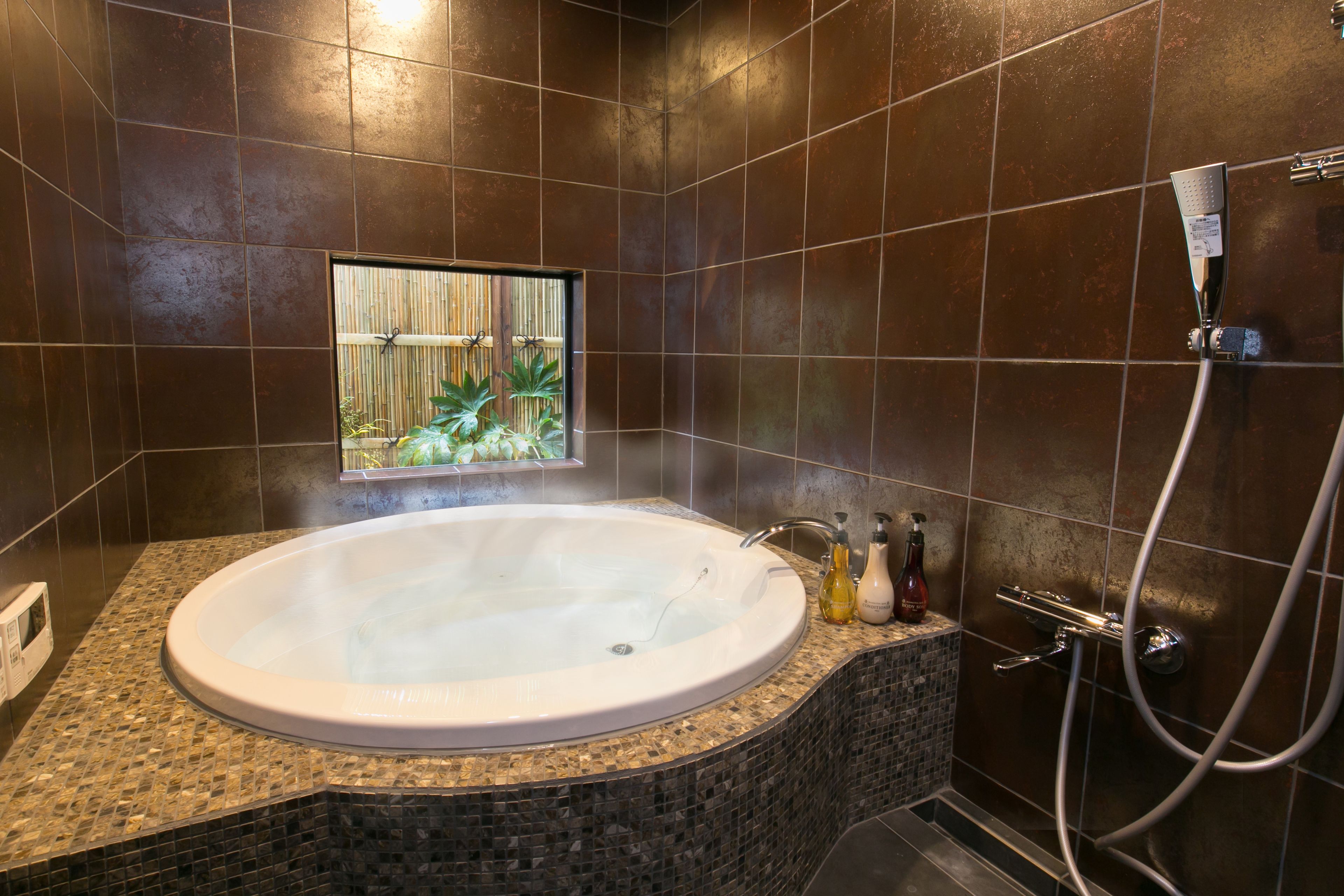 A modern bathroom with a large bathtub, a shower area, and a small window with plants.