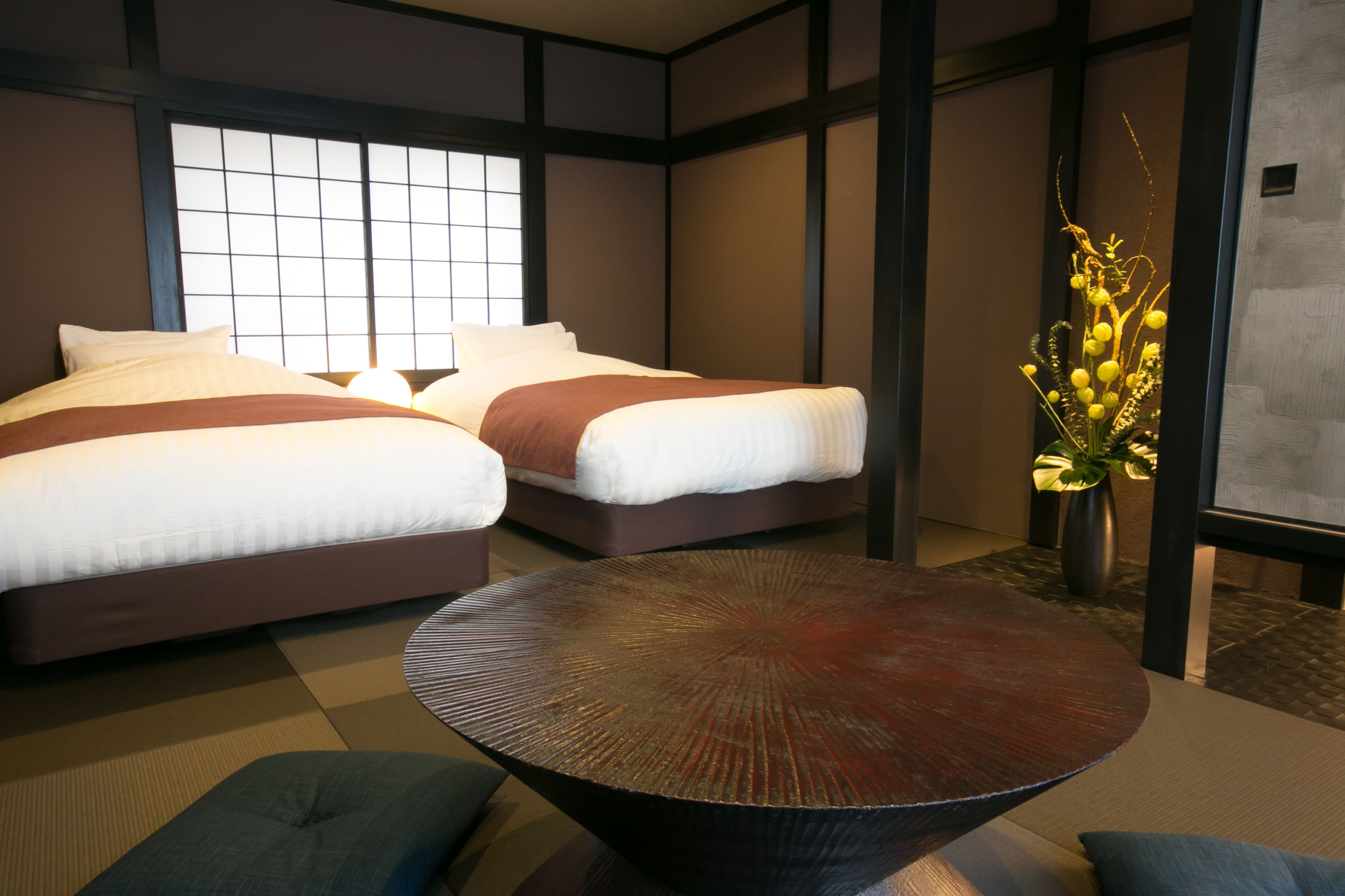 A hotel room with two beds, a round table, and a decorative plant.