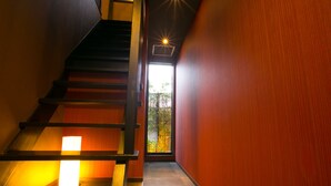 Un interior moderno con una escalera de madera, una pared roja y vistas al verdor exterior.