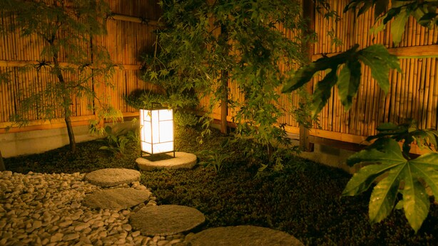 Un jardín japonés tradicional con un farol, pared de bambú y piedras para caminar.