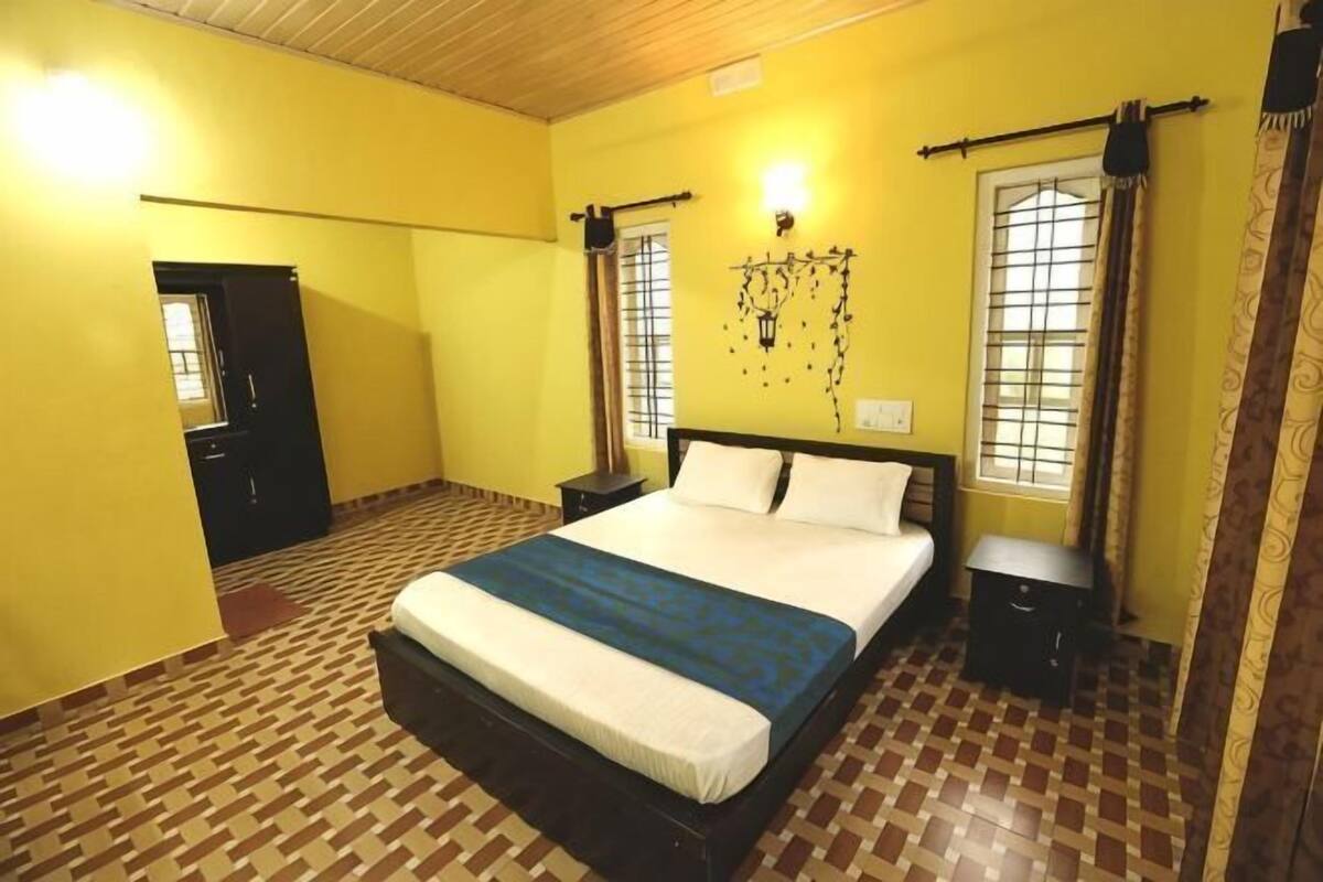 A bedroom with a bed, a nightstand, a window with curtains, a door, and a patterned floor.