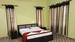 A single bed with a wooden headboard in a room with patterned floor tiles and curtains on the windows. - Himadri Retreat Cottages (Vythiri)