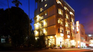 Un hotel de varios pisos con ventanas e balcones iluminados, rodeado de palmeras.