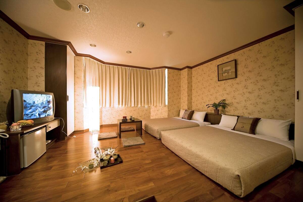 A hotel room with a television, two beds, a desk, and a small table.
