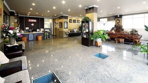 Un hall de hotel con mostrador de recepción, zona de estar y plantas decorativas.