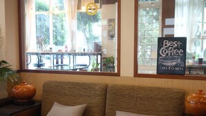 Un rincón acogedor con un sofá y cojines, una ventana con vistas al exterior, y un cartel que anuncia el mejor café de la ciudad.