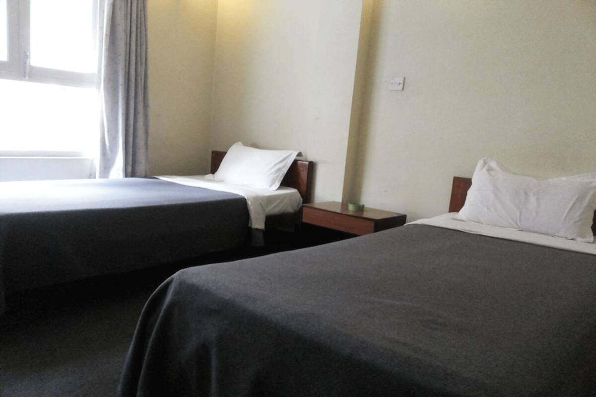 A hotel room with two single beds, a nightstand, and a window with curtains.