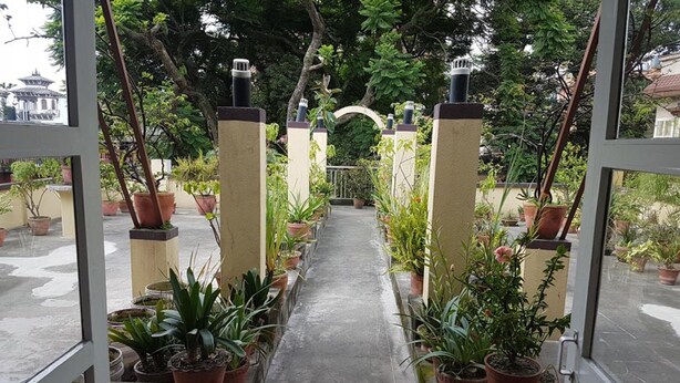 A pathway lined with potted plants leading to a traditional gate, surrounded by lush greenery. - Imperial Guest House (Kathmandu)