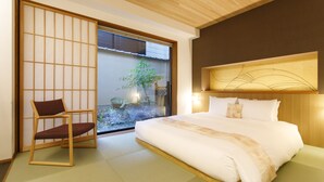 A hotel room with a large bed, a wooden chair, a sliding shoji screen, and a view of a garden through a glass door. - Gion Misen Furumonzen (Kyoto)
