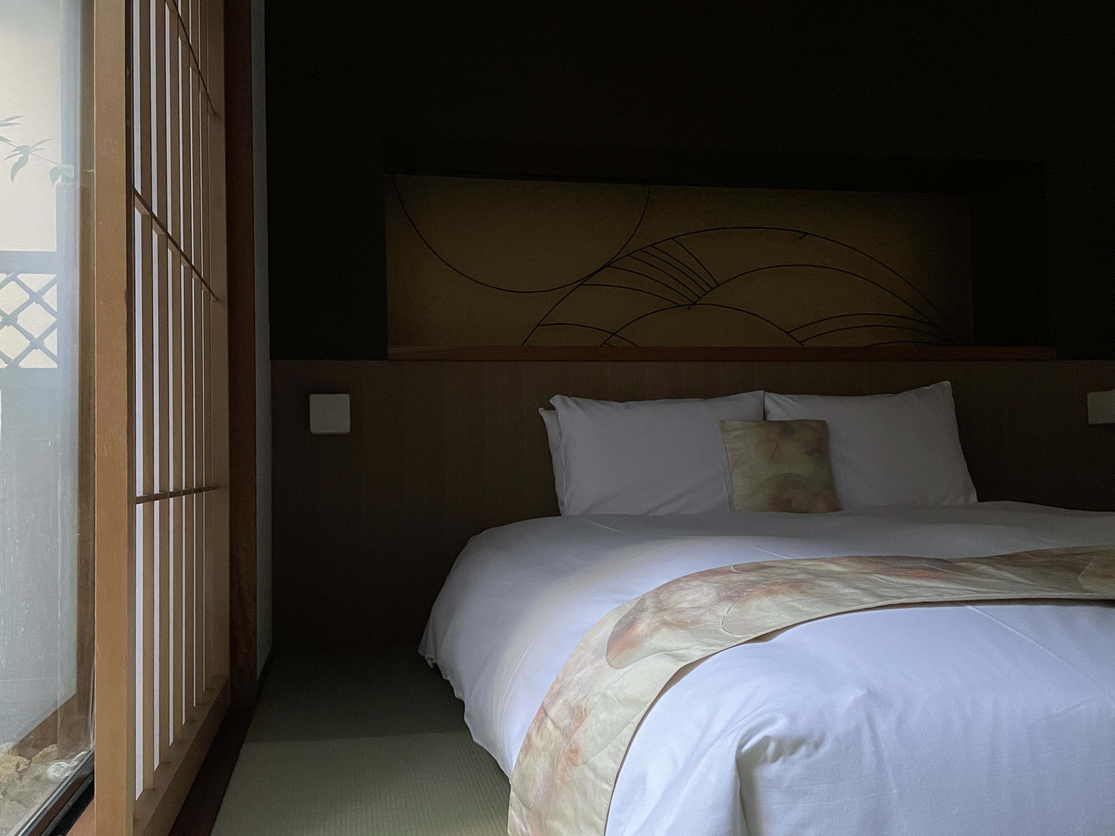 Une chambre d’hôtel comprenant un lit, une tête de lit ornée d’un motif décoratif, une fenêtre donnant sur l’extérieur et un interrupteur fixé au mur.