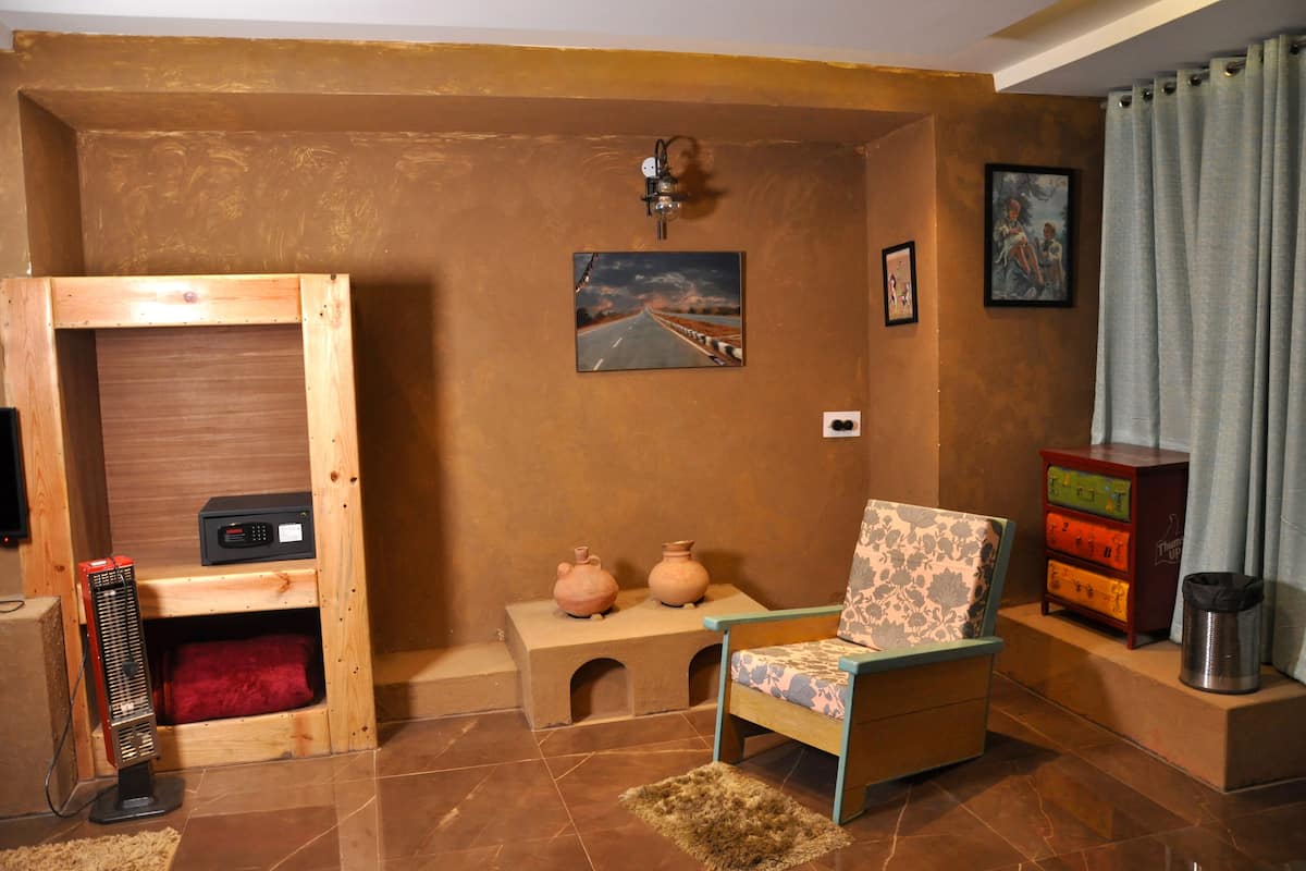 A compact room with a wooden bed, a small table with pottery, a chair, a heater, and a picture of a road on the wall.