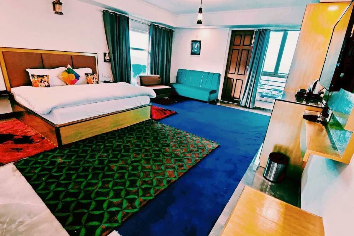 A hotel room with a bed, a sofa, a desk, and a view of the outside.