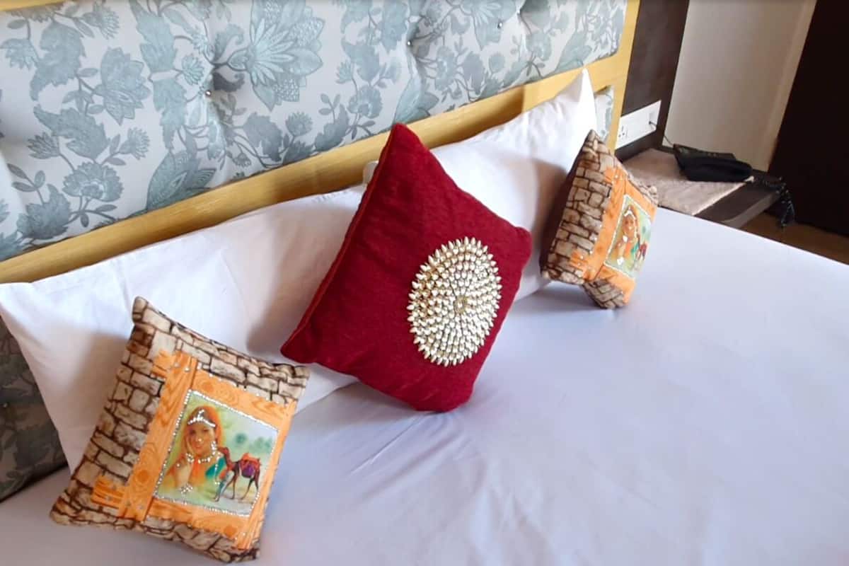 A bed with a floral-patterned headboard, white bedding, and decorative pillows with a central image and a red pillow with a gold design.
