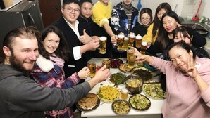 Un groupe de personnes trinquant avec des verres de bière autour d’une table où se trouvent divers plats.