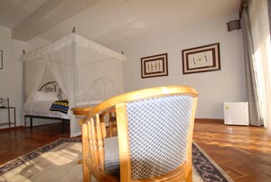 Un dormitorio con cama de dosel, una silla de madera con cojín estampado, y dos cuadros en la pared.