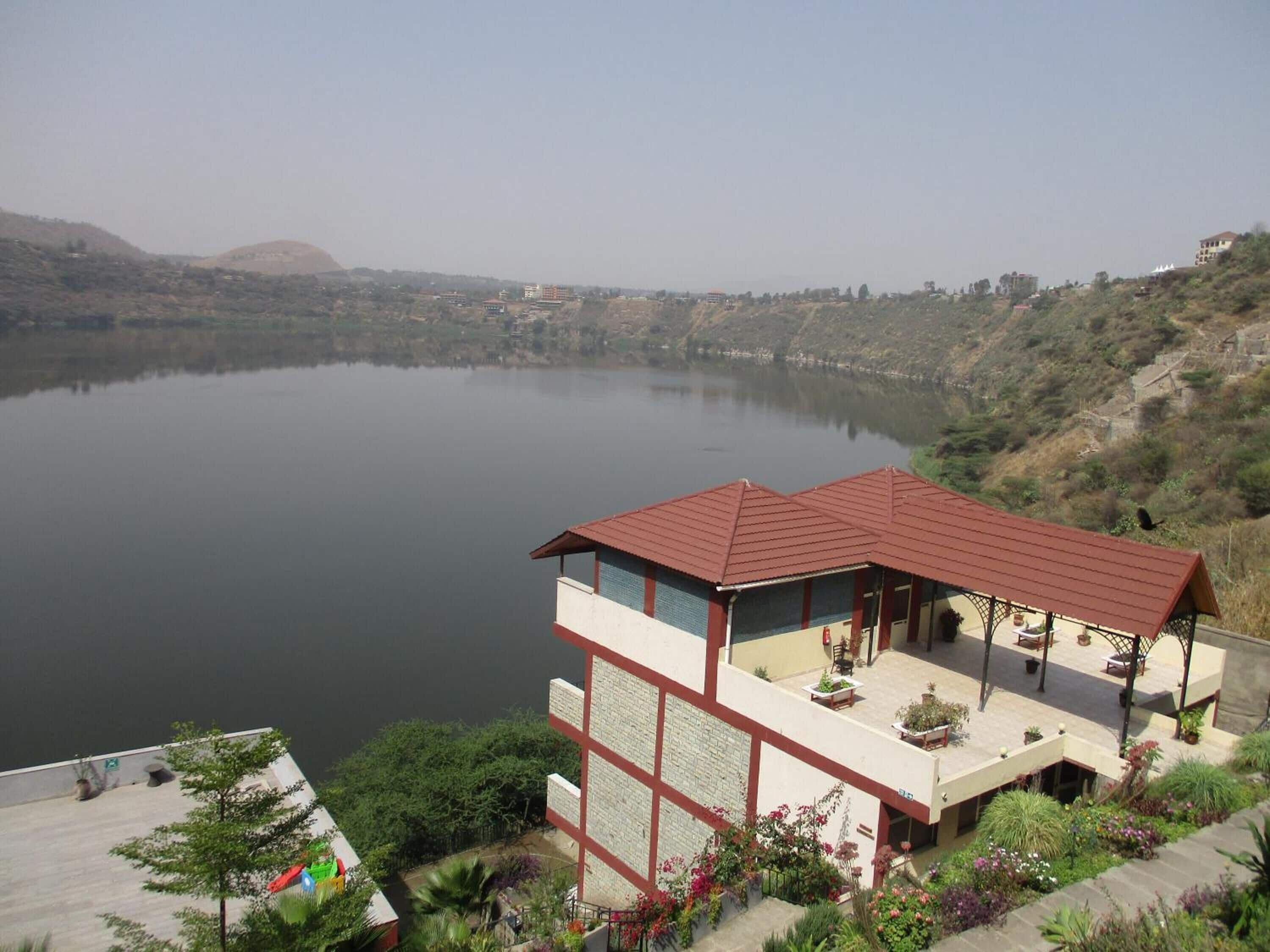 A two-story building with a red roof, a balcony with seating, and a view of a lake.