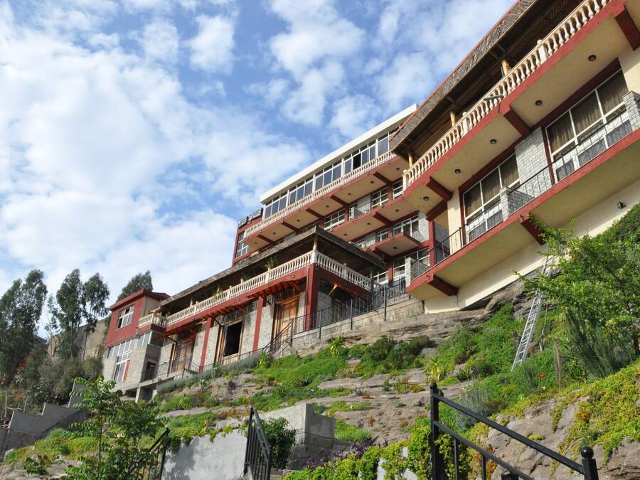 A multi-story hotel with balconies, situated on a hillside with lush greenery.