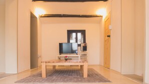 A room with a flat-screen TV on a stand, a wooden bench, and a small table with a vase.