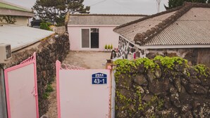 A traditional house with a tiled roof, a stone wall, and a pink gate.