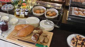 A breakfast buffet with various breads, pastries, and condiments.