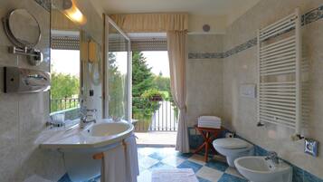 A bathroom with a large sink, a bidet, and a toilet. There is a window with a view of greenery outside.