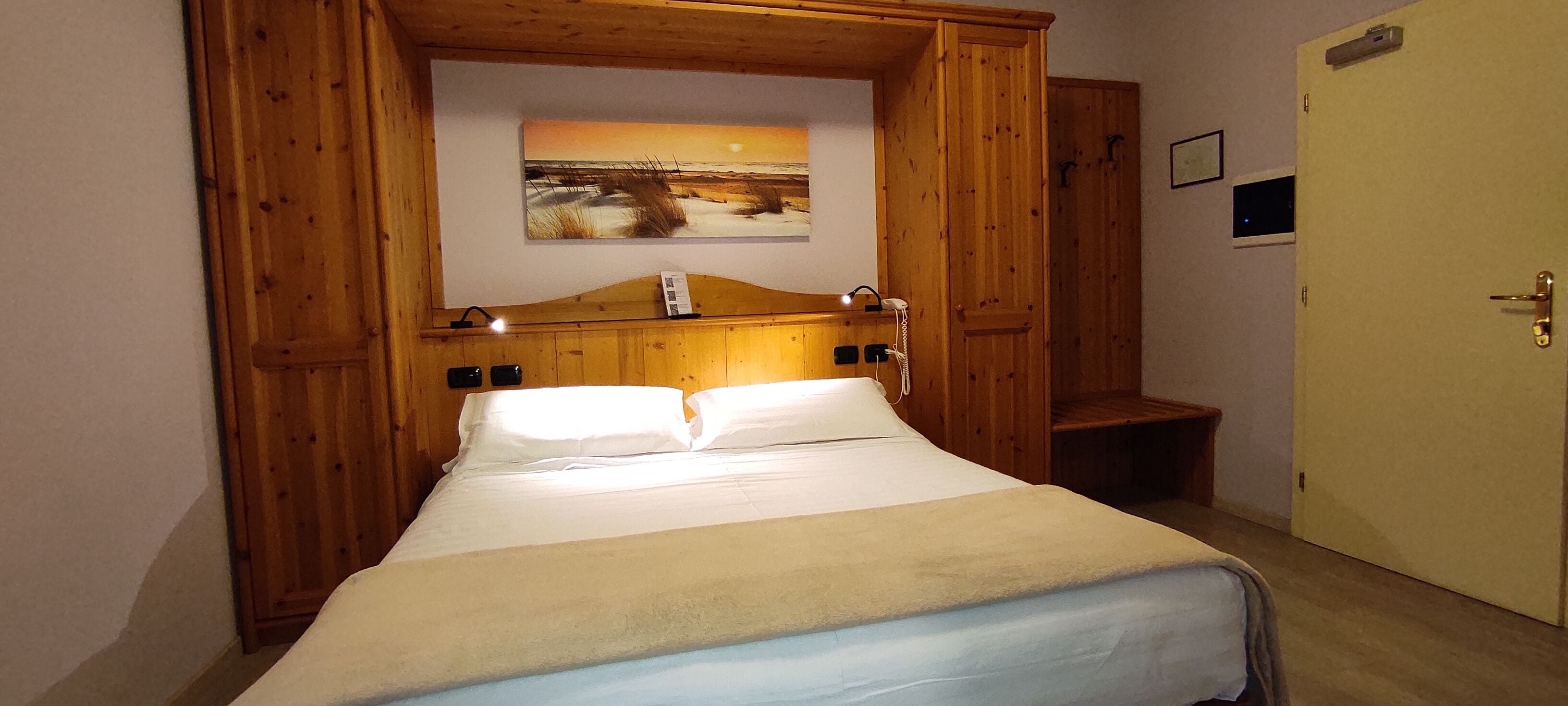 Un dormitorio con estructura de madera, una cama, una mesita de noche, un banco y un cuadro en la pared.