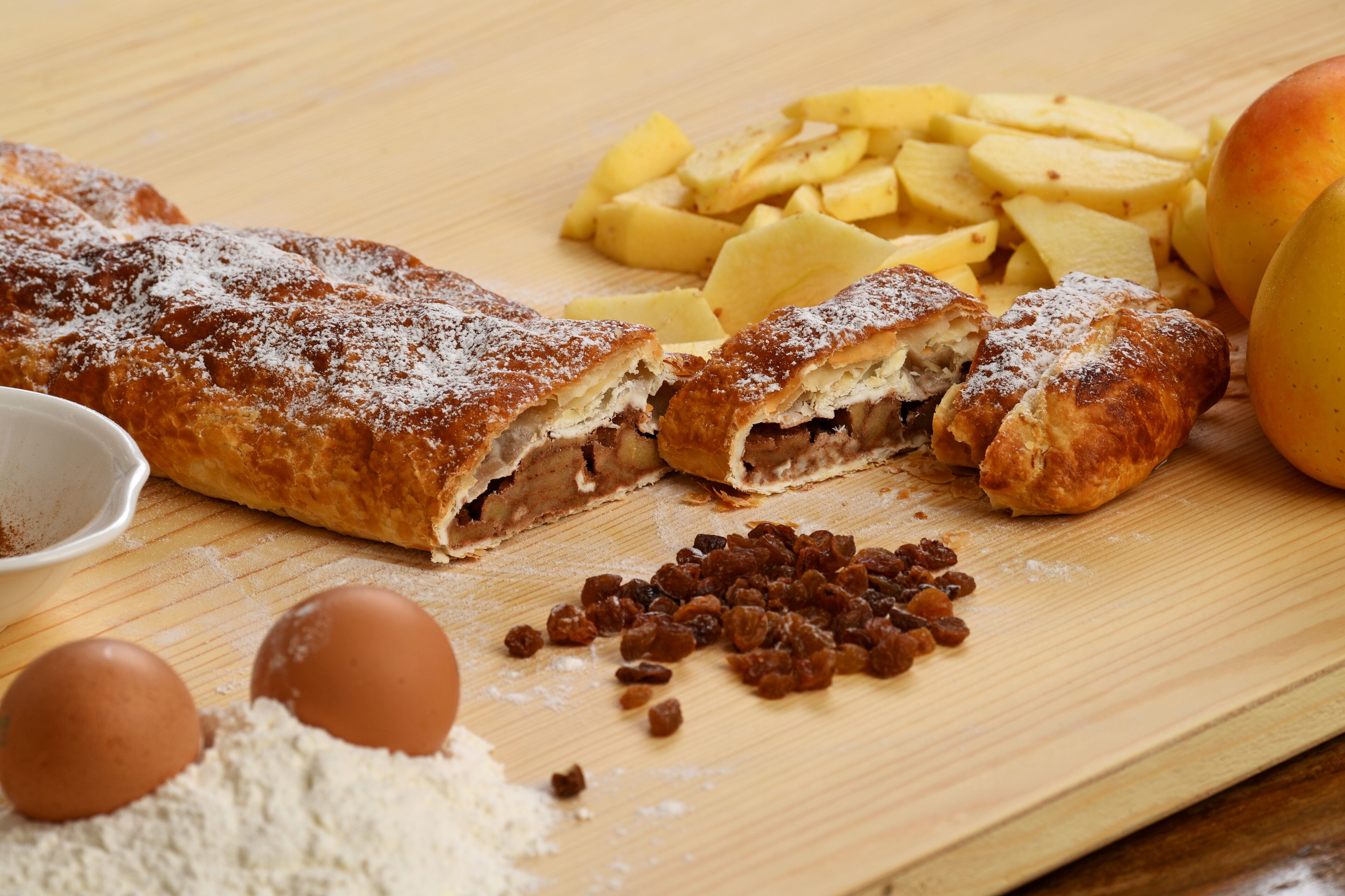 A pastry with apple slices and raisins on a wooden surface.