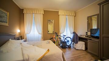 Habitación de hotel con una cama, un escritorio con televisor, una bicicleta y un espejo.