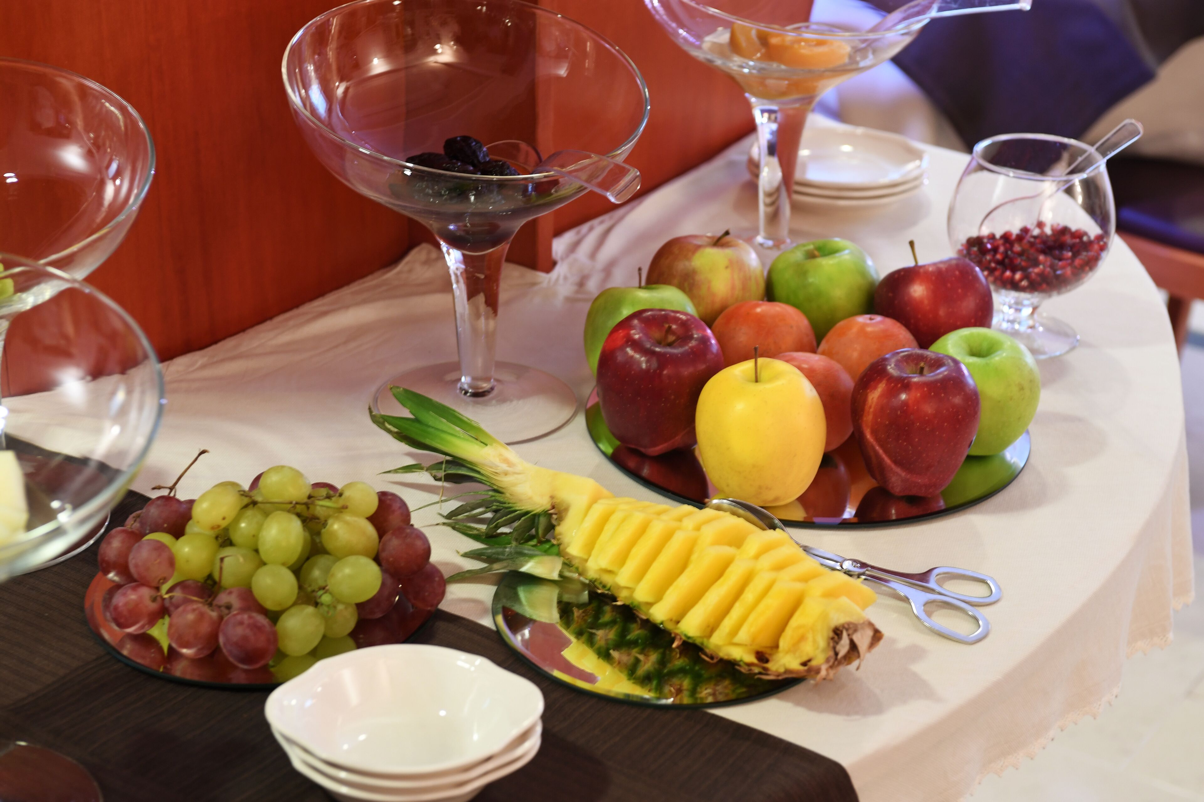 A table with a variety of fruits and a pineapple on a white tablecloth.