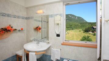 Un bagno con un lavandino capiente, uno specchio e una finestra che si affaccia su un paesaggio verde.
